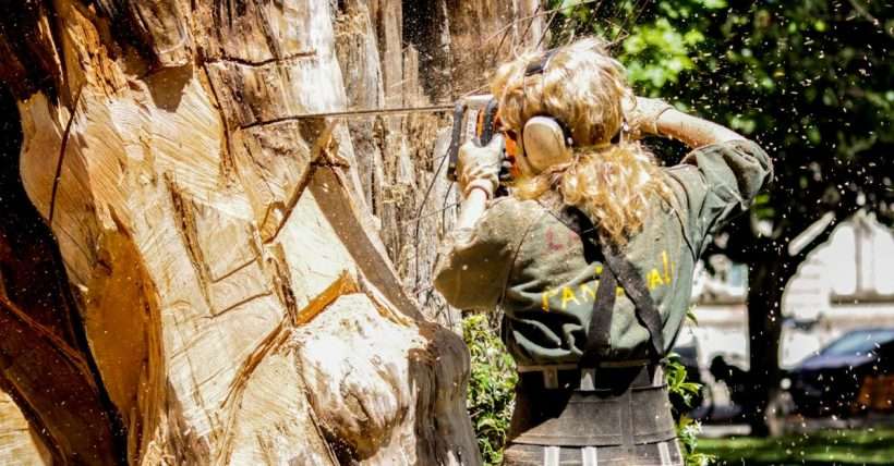 A skilled woman arborist cuts a large tree with a chainsaw outdoors, showcasing expertise in tree care.